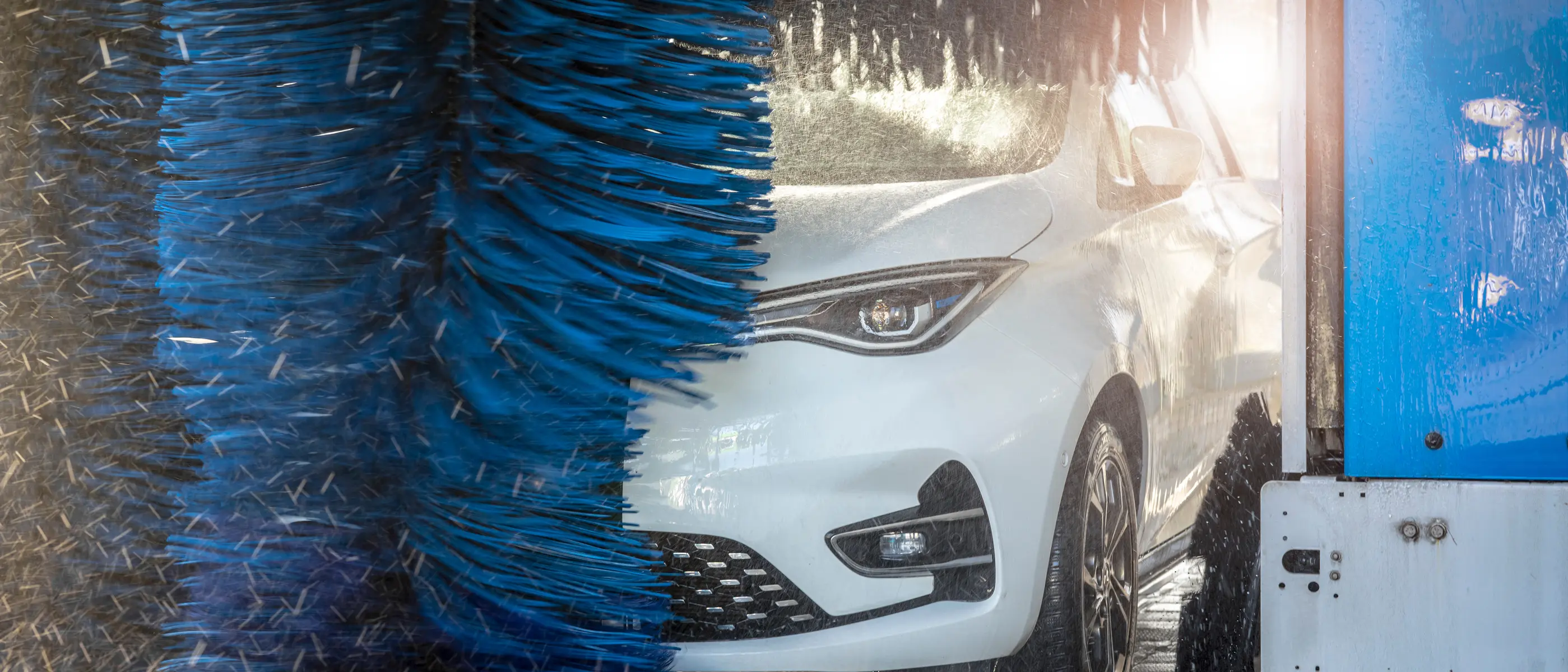 Ein weißes Auto mit reflektierendem Lack wird von blauen Bürsten in der Waschanlage gereinigt