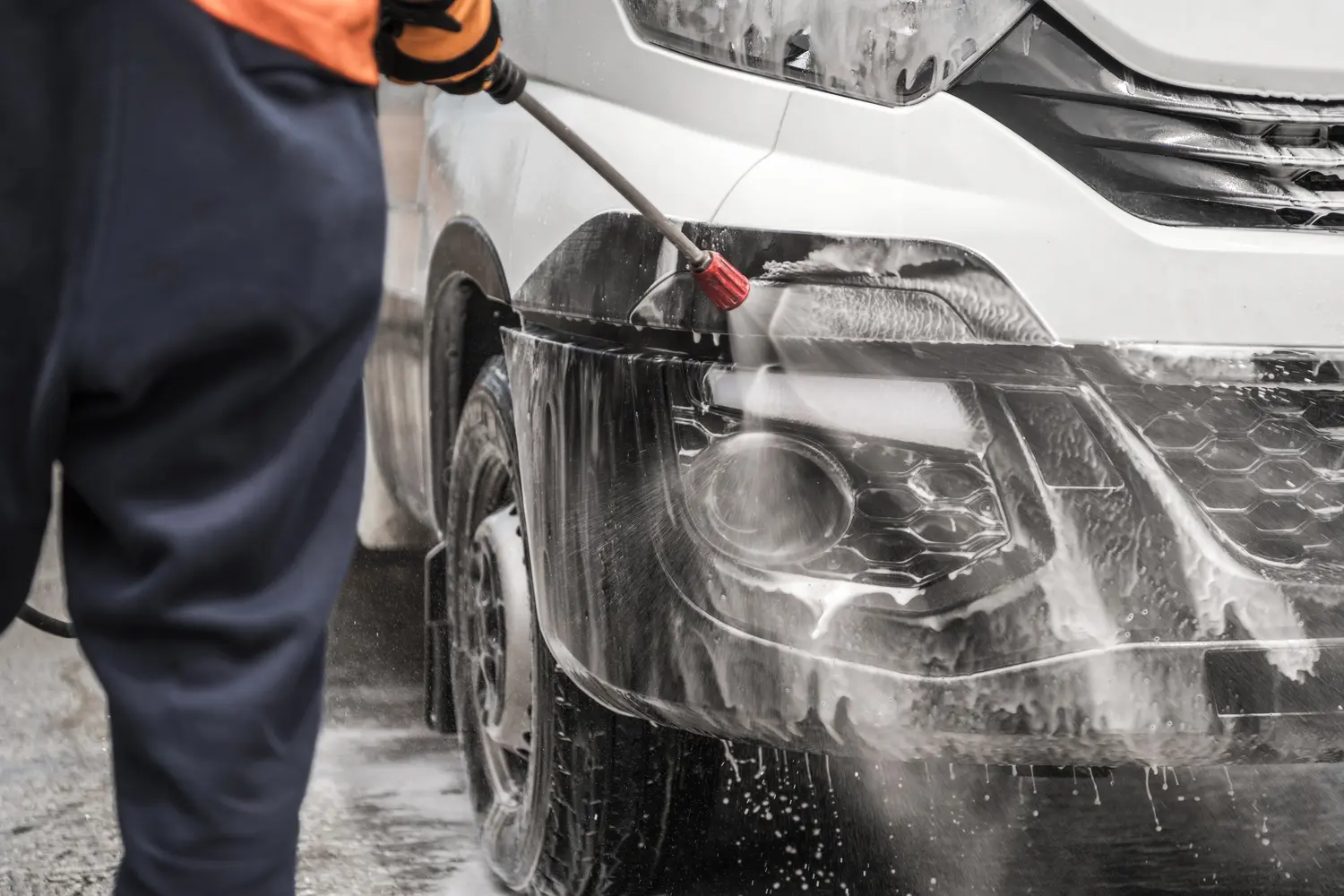 Eine Person spritzt lächelnd weißen Schaum auf die Front eines silbernen Autos